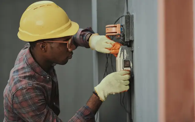Eletricista com capacete fazendo manutenção em caixa elétrica externa